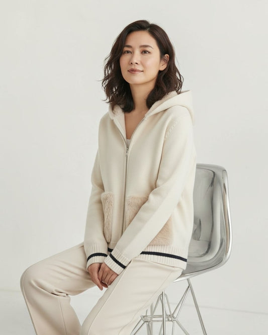FAVEUR Fauxファー付きニットフーディー オフホワイトの着用イメージ、椅子に座ったモデルの全身カット