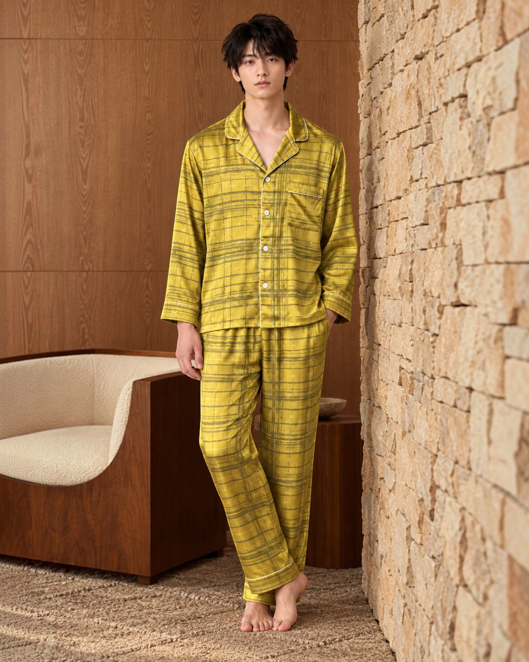 Boutique HANAYA × Foo Tokyo イチョウゴールドのシルクパジャマ、石壁の横に立つ男性モデルの全身着用姿、開襟トップスの胸ポケットとパイピング